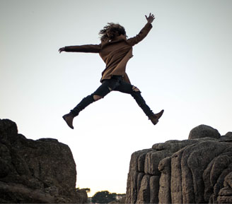Girl jumping of a gap between two rocky cliffs